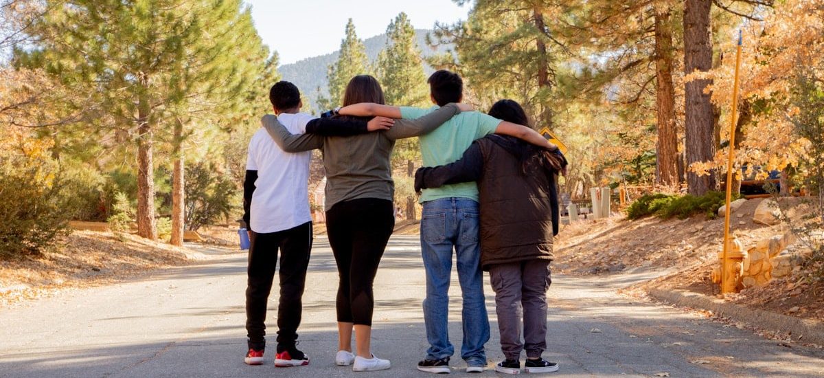 four people with hands on shoulders standing on road during daytime