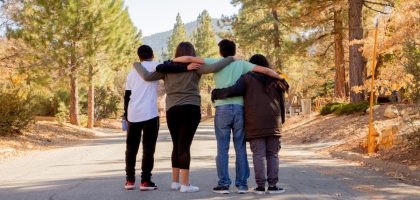 four people with hands on shoulders standing on road during daytime
