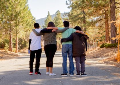four people with hands on shoulders standing on road during daytime
